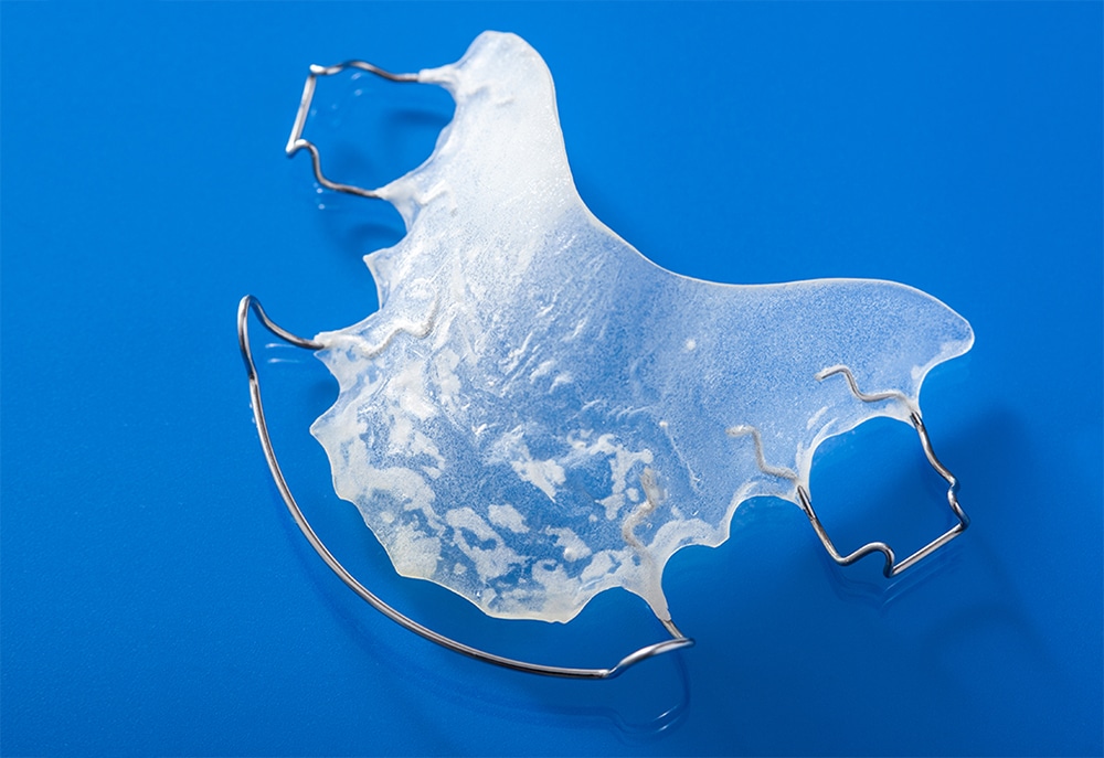 Close-up of a clear plastic and wire dental retainer on a blue background