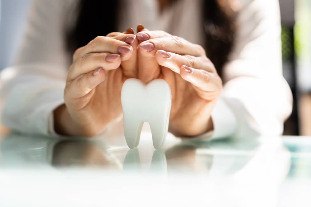 Close-up of hands gently cupping a tooth-shaped model on a glass surface, symbolizing dental care