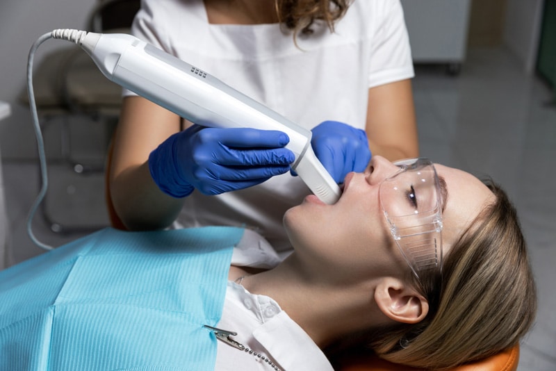 A dentist using a Medit scanner to take a digital dental impression from a patient wearing protective glasses in a dental chair